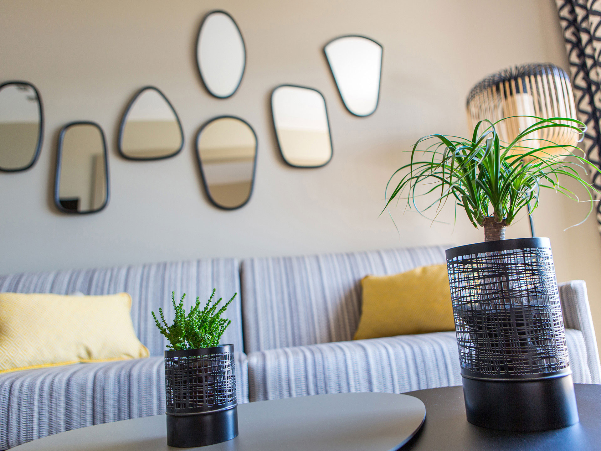 Coin salon moderne d’hôtel avec canapé rayé, plantes décoratives et miroirs muraux