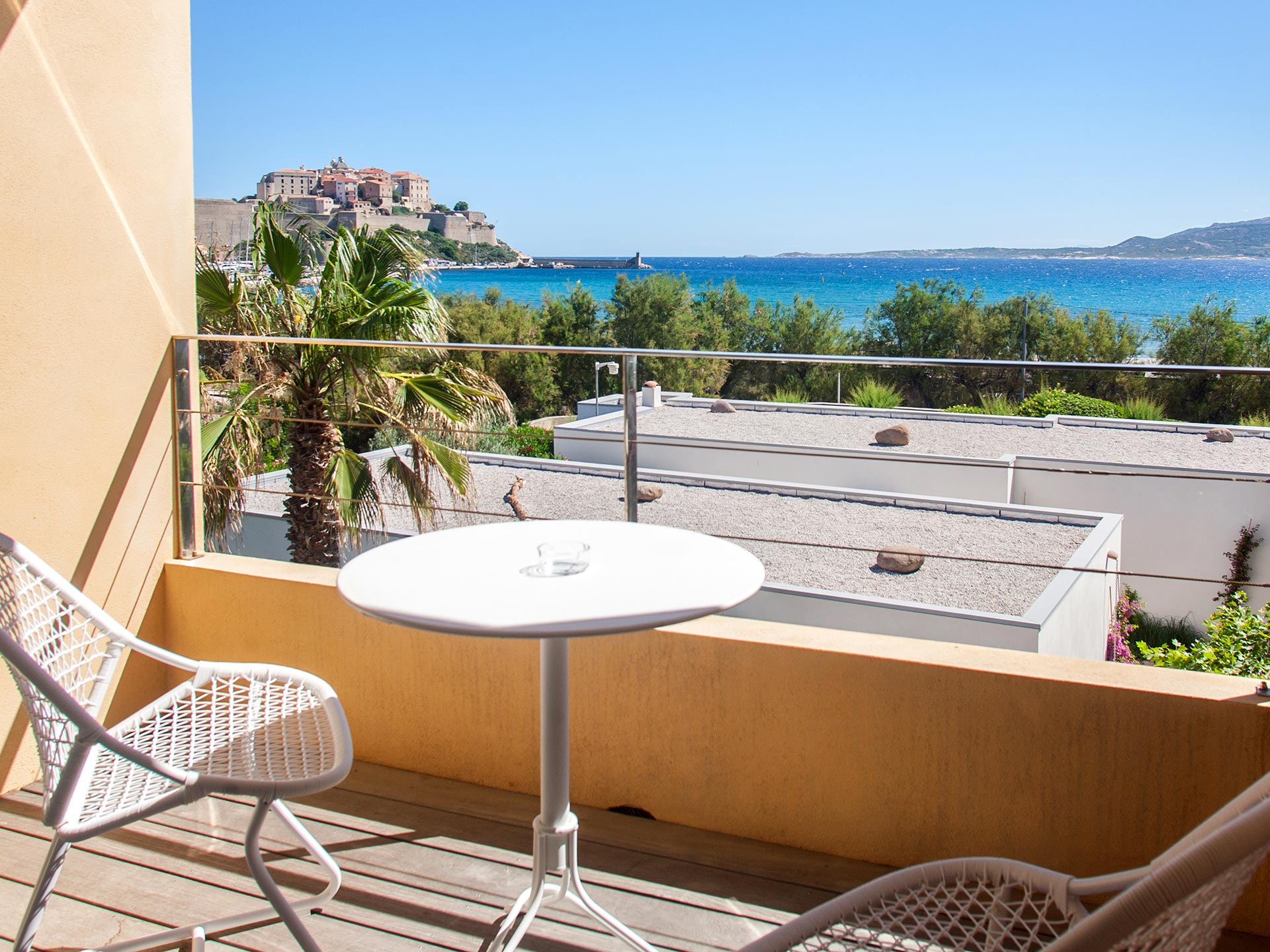 Balcon d’hôtel avec table blanche et vue sur la mer et la citadelle de Calvi