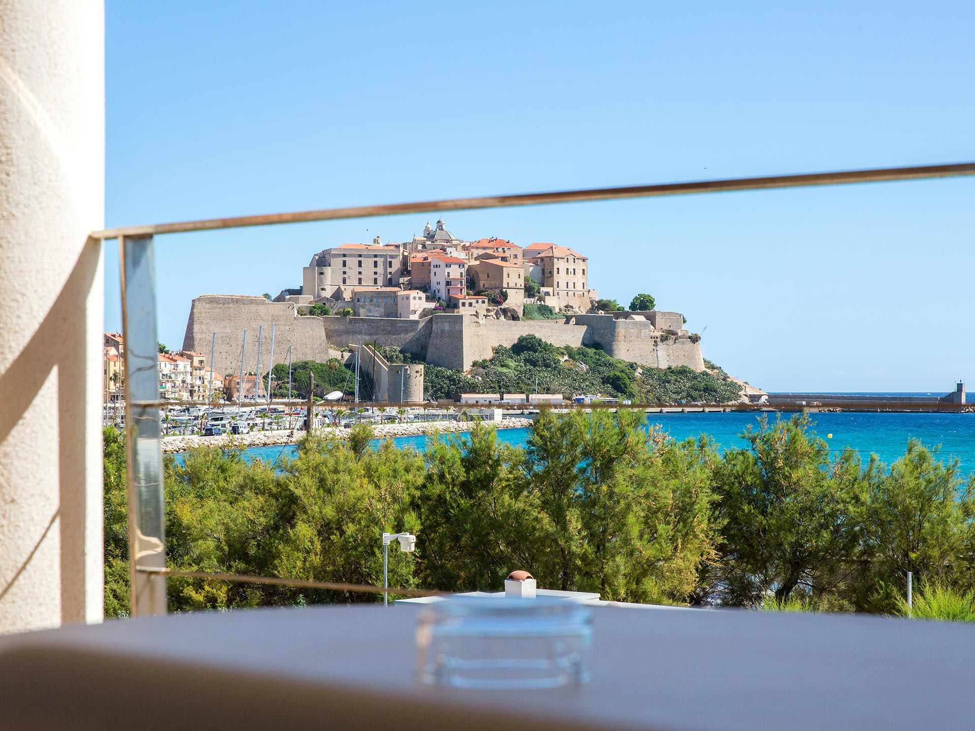 Vue depuis la terrasse de l’hôtel sur la citadelle de Calvi, le port et la mer turquoise