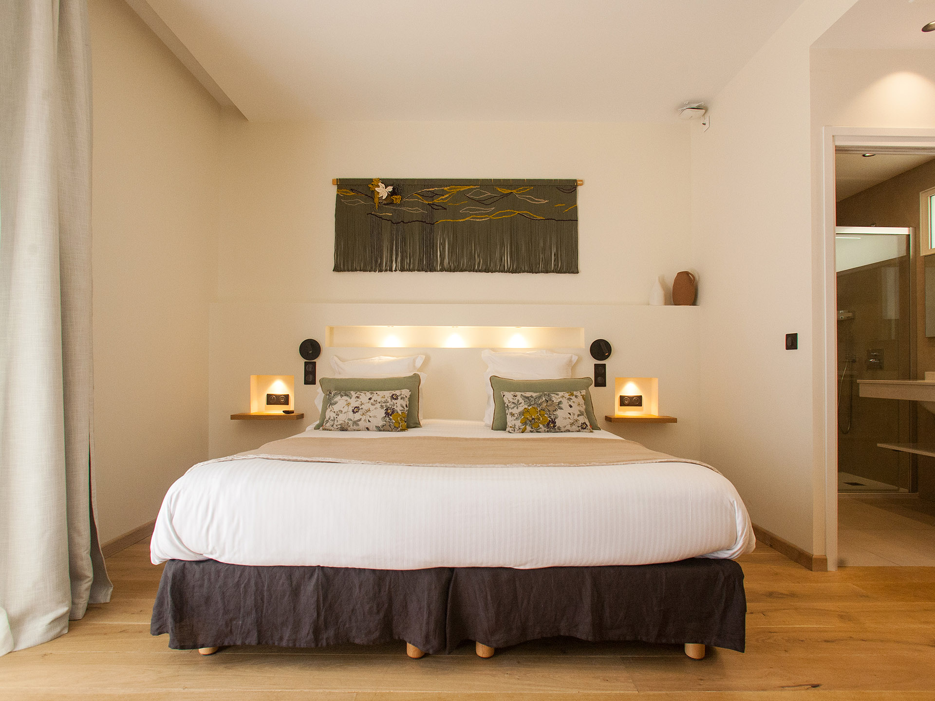 Chambre d’hôtel moderne avec lit double, décoration naturelle et salle de bain attenante